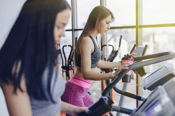 Девушки в тренажерном зале тренируются на беговых дорожках и пьют воду, улыбаясь
