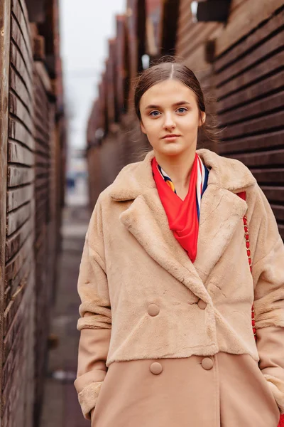 Joven elegante linda chica en un abrigo de piel paseando por la ciudad cerca de casas de madera y paredes de piedra — Foto de Stock