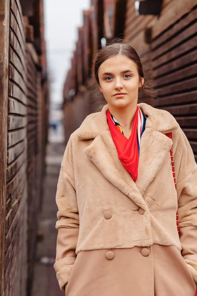 Joven elegante linda chica en un abrigo de piel paseando por la ciudad cerca de casas de madera y paredes de piedra — Foto de Stock
