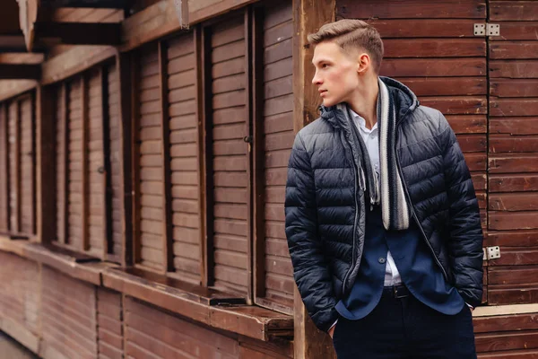 Giovane ragazzo elegante con un volto monumentale passeggiate in una città fresca vicino ai muri di legno e pietra — Foto Stock