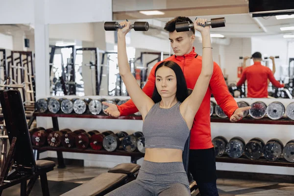 Bir genç kız bir spor salonunda spor giyim giyiyor halter alıştırmalar gerçekleştirir, Koç ona yardımcı olur