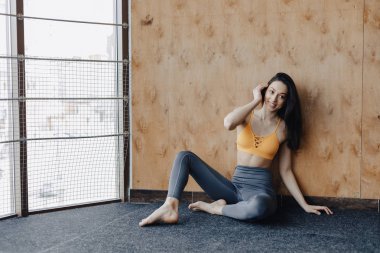 Genç çekici Fitness kız yoga dersleri dinlenme, ahşap bir duvarın arka planda pencerenin yakınında yerde oturuyor