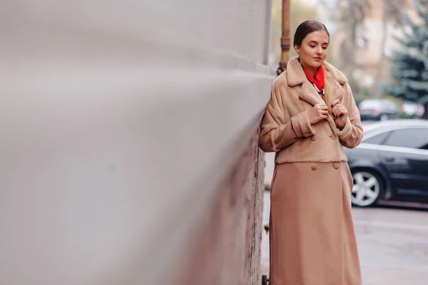 Giovane ragazza carina elegante in una pelliccia passeggiando per la città vicino a case di legno e muri di pietra — Foto Stock