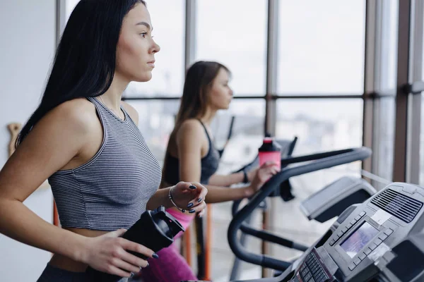 Kızlar spor salonunda koşu bandı ve içecek su, eğitimli gülümseyen