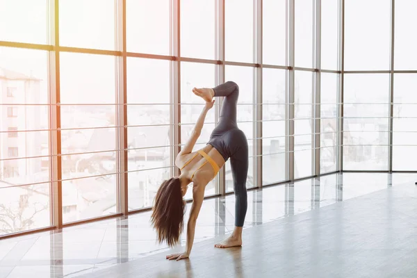 Chica atractiva joven haciendo ejercicios de fitness con yoga en el suelo contra el fondo de ventanas panorámicas — Foto de Stock