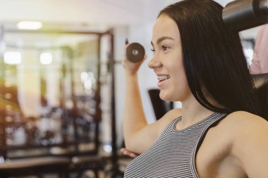Bir genç kız bir spor salonunda spor giyim giyiyor halter alıştırmalar gerçekleştirir, Koç ona yardımcı olur