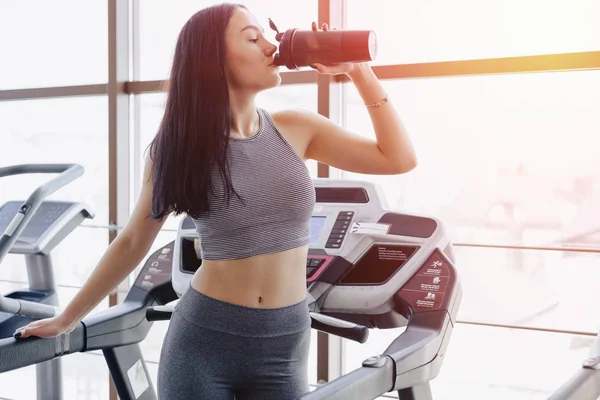 Girl in the gym are trained on treadmill and drink water
