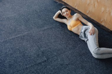 Genç çekici Fitness kız yoga dersleri dinlenme, ahşap bir duvarın arka planda pencerenin yanında yerde yatıyor