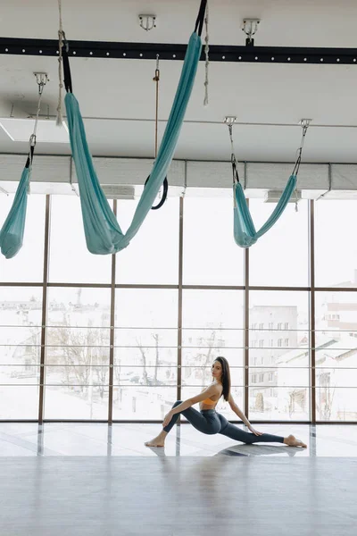 Jonge aantrekkelijke meisje doet fitness oefeningen met yoga op de vloer tegen de achtergrond van panoramische ramen — Stockfoto