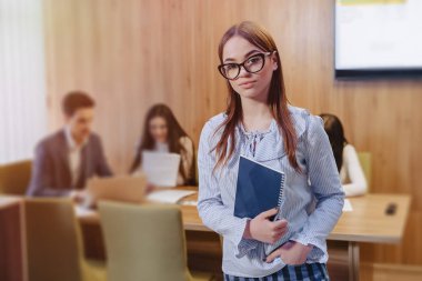çalışan meslektaşlarının arka planda elinde bir dizüstü bilgisayar ile gözlük genç çekici şık ofis çalışanı kız