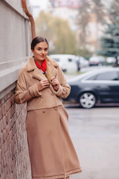 Young stylish cute girl in a fur coat strolling around the city near wooden houses and stone walls — Stock Photo, Image