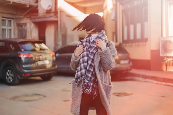 Приваблива позитивна молода дівчина в окулярах на пальто на тлі будівель на машинах — стокове фото