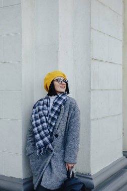 Basit bir ışık arka planda ceket ve sarı Beret gözlüklerini çekici gülümseyen genç kız