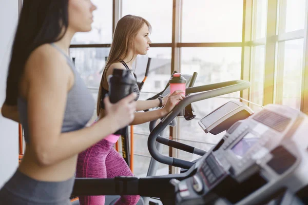 Kızlar spor salonunda koşu bandı ve içecek su, eğitimli gülümseyen
