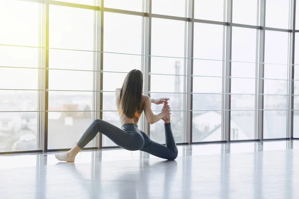 Mladá přitažlivá dívka provádí fitness cvičení s jóga na podlaze na pozadí panoramatických oken — Stock fotografie