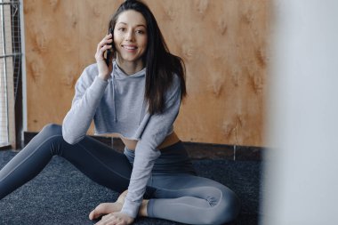Genç çekici Fitness kız ahşap bir duvarın arka planda pencerede yakın katta oturan, yoga dersleri dinlenme ve telefonda konuşurken