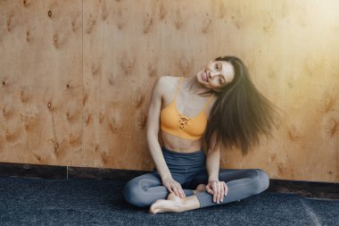 Genç çekici Fitness kız yoga dersleri dinlenme, ahşap bir duvarın arka planda pencerenin yakınında yerde oturuyor