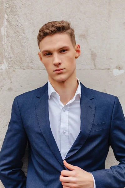 Young stylish guy with a monumental face walks in a cool city near the wooden and stone walls — Stock Photo, Image