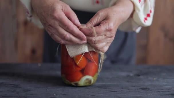 Eine alte Frau in traditioneller ukrainischer Kleidung wickelt eine Dose Tomaten in ein Sacktuch — Stockvideo