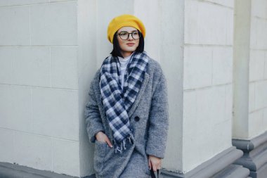 Basit bir ışık arka planda ceket ve sarı Beret gözlük çekici genç kız