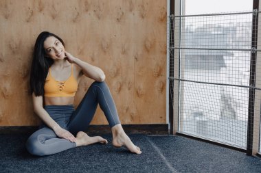 Genç çekici Fitness kız yoga dersleri dinlenme, ahşap bir duvarın arka planda pencerenin yakınında yerde oturuyor