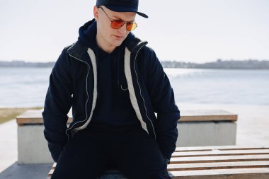 turuncu gözlük, ceket ve kap şık genç çocuk, ilkbahar veya sonbaharda göl etrafında yürümek