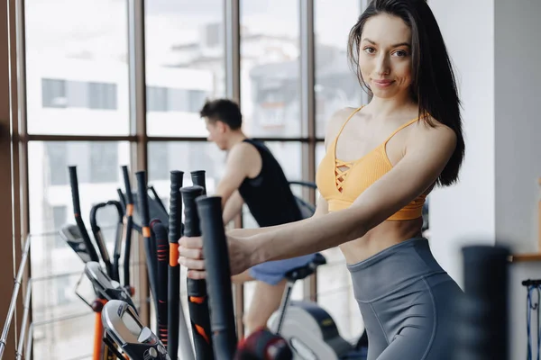 Chica atractiva joven en el gimnasio en bicicleta estática, fitness y yoga — Foto de Stock