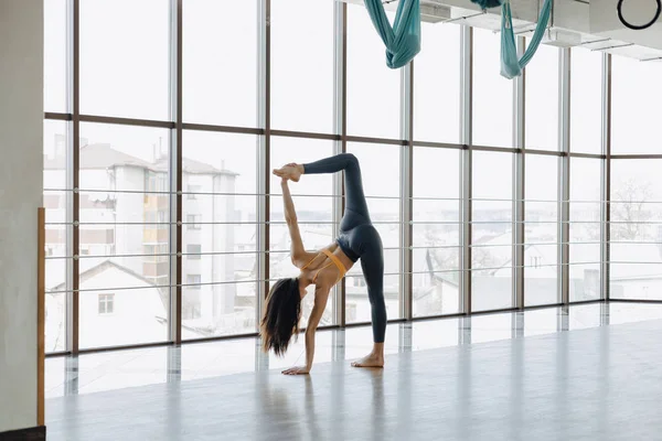 Chica atractiva joven haciendo ejercicios de fitness con yoga en el suelo contra el fondo de ventanas panorámicas — Foto de Stock