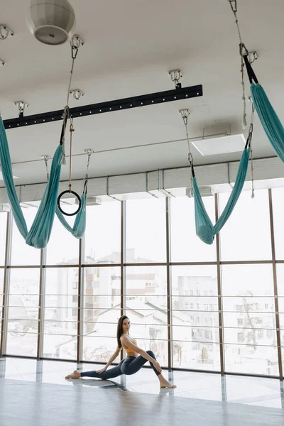 Jonge aantrekkelijke meisje doet fitness oefeningen met yoga op de vloer tegen de achtergrond van panoramische ramen — Stockfoto
