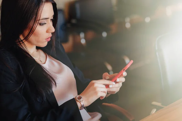 Joven chica emocional atractiva en ropa de estilo de negocios sentado en el escritorio con teléfono en la oficina o la audiencia — Foto de Stock