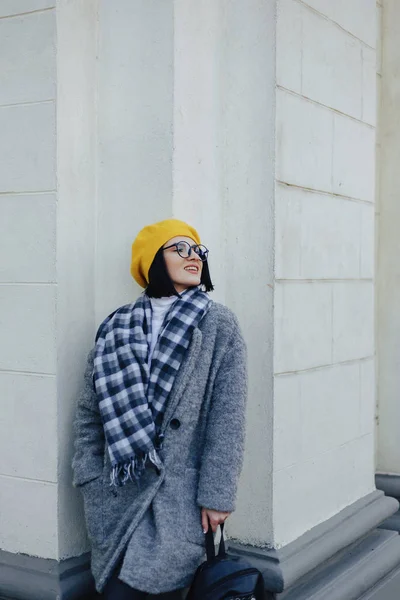Приваблива усміхнена молода дівчина в окулярах в пальто і жовтий Берет на простому світлому фоні — стокове фото