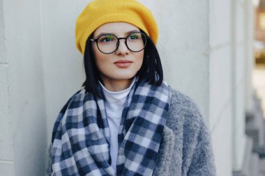 Basit bir ışık arka planda ceket ve sarı Beret gözlük çekici genç kız