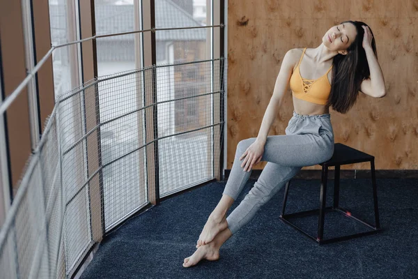 Genç çekici Fitness kız sandalye üzerinde ahşap bir duvarın arka planda pencerenin yakınında oturan, yoga dersleri dinlenme