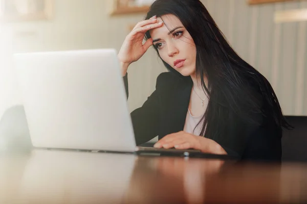 Ofis veya oditoryumda bir dizüstü bilgisayar ve telefon bir masada oturan iş tarzı giysiler genç çekici duygusal kız