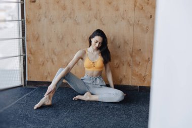 Genç çekici Fitness kız yoga dersleri dinlenme, ahşap bir duvarın arka planda pencerenin yakınında yerde oturuyor