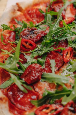 Jambon, peynir, Arugula, fesleğen, domates, pepperoni biber ile Napoliten Baharatlı pizza metin için bir yer ile bir hücrede bir masa örtüsü üzerinde bir ahşap tahta üzerinde peynir ile püskürtülmüş
