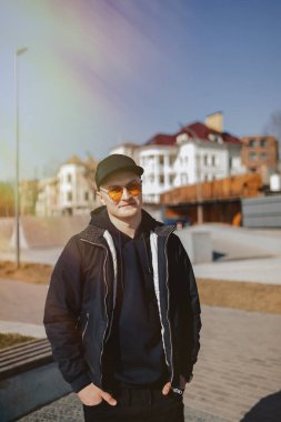 turuncu gözlük, ceket ve kap şık genç çocuk, ilkbahar veya sonbaharda göl etrafında yürümek