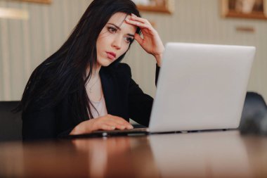 Ofis veya oditoryumda bir dizüstü bilgisayar ve telefon bir masada oturan iş tarzı giysiler genç çekici duygusal kız