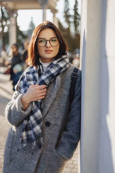 Attraktive junge Mädchen mit Brille im Mantel, die an einem sonnigen Tag spazieren gehen — Stockfoto