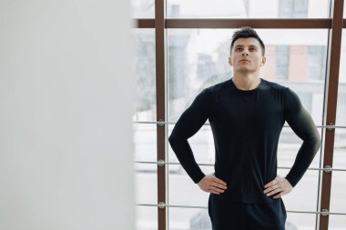 Pencere kenarındaki çekici sporcu. Sporcu geniş pencerelerin yanında poz veriyor. Spor ve spor. güneşli.
