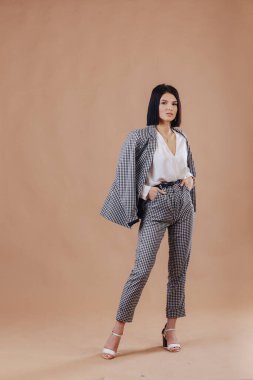 Stüdyoda krem rengi arka planda poz veren iş elbiseli çekici, şık bir genç kız. Şık kıyafetler ve entelektüellik kavramı.