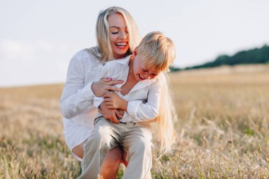 Sarışın küçük çocuk samanlı, beyaz saçlı annesiyle oynuyor. Yaz, güneşli hava, çiftçilik. Mutlu çocukluk. aile.