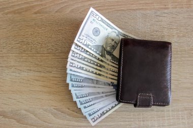 Deri cüzdanın altında dolar banknotları var. Dolarlar ofisteki bir cüzdanın altındaki ahşap bir masada yatıyor..