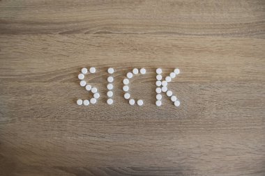 Hasta kelimesi ahşap bir masaya yayılmış. Klinikteki masada beyaz haplarla konuşuluyor..