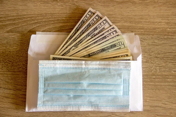 Hastalık maskesi dolar üzerine kuruludur ve onu korur. Dolarlar tıbbi maske ile korunan bir zarfın üzerinde duruyor..