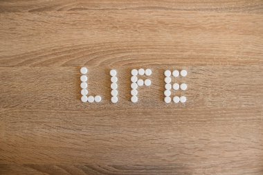 Hayat kelimesi masada beyaz haplarla doludur. Yaşam ve ölümün sembolü olarak haplı hayat sözü masada yatıyor..