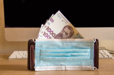 Cüzdan bilgisayarın yanındaki ofisteki masanın üzerinde. Tıbbi maske cüzdanı ve parayı koronavirüsten korur.. 