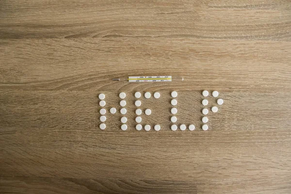 The word help is laid out on a wooden table. The word help with white pills lies on a wooden table.