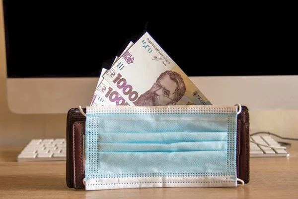 Para dolu cüzdan ofisteki ahşap bir masanın üzerinde duruyor. Bilgisayarın yanındaki cüzdanda Ukrayna Hryvnia 'sı.