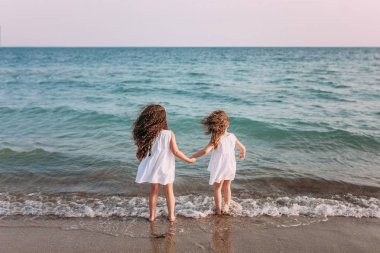 Beyaz elbiseler içinde iki kız sahilde deniz köpüğü duruyorsun